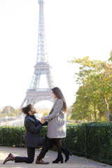 Afro american happy man making proposal to caucasian girlfriend in Paris, Eiffel Tower in...