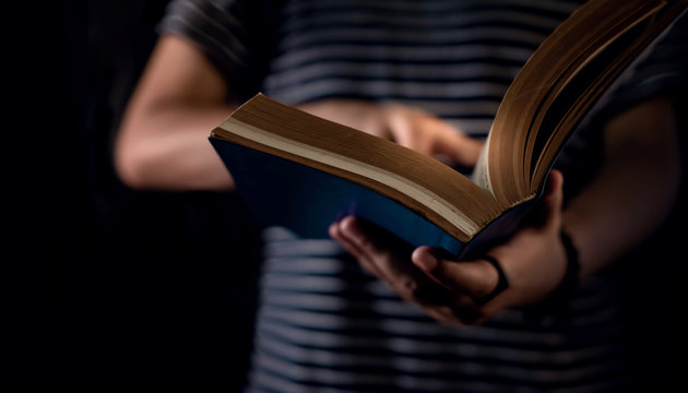 Reading Concept. Person Holding Opened Bible Book on Hand. Dark Tone, Cropped image