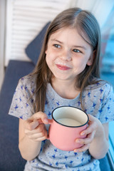 Closeup portrait of a cute little girl with a white milk mustache, pleased charming child with a smile holds a glass, drinks milk before bedtime