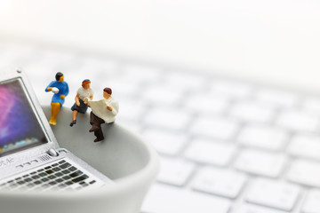 Miniature people sitting on cup of coffee with keyboard and laptop.