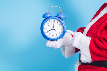 Santa Claus holding alarm clock on blue background, Christmas arrival concept