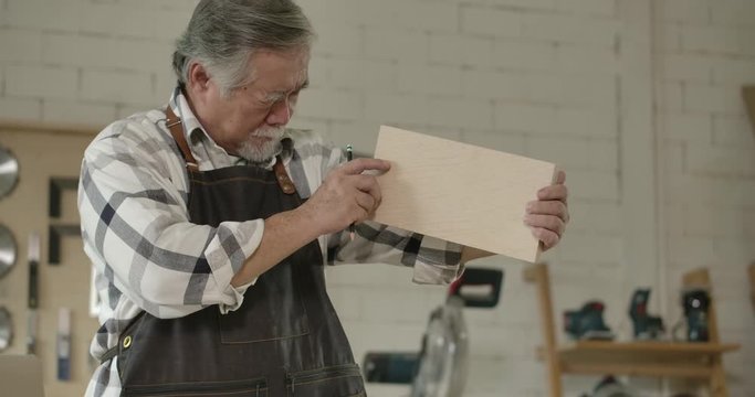 Asian senior carpenter works in carpentry workshop during the day.