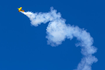 Vintage biplane does stunt with smoke trails in the blue sky.