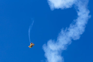 Vintage biplane does stunt with smoke trails in the blue sky.