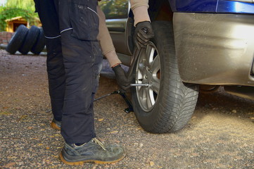 Process of maintenance in autumn. man is changing tire with wheel wrench. Replacement of winter and...