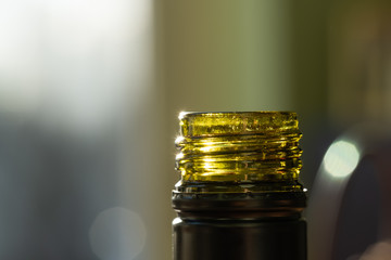 Close-up, shallow focus of an opened glass wine bottle, showing detail of the green glass and screw thread of the bottle top. Shown within a restaurant area,