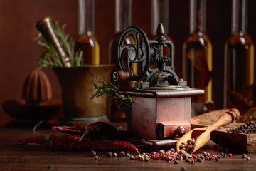 Old pepper mill with cooking utensils, bottles of olive oil, spices and rosemary on a wooden table.