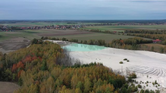 Aerial view of open pit kaolin clay mine (kaolinite quarry) with turquoise pool of water surrounded by autumn landscape with colorful trees - landscape panorama of Poland from above, Europe