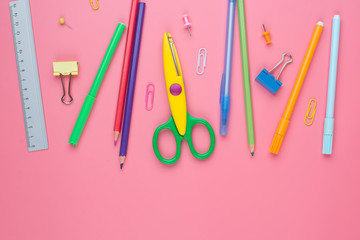 Colorful school supplies over a paper on pink background with place for your text