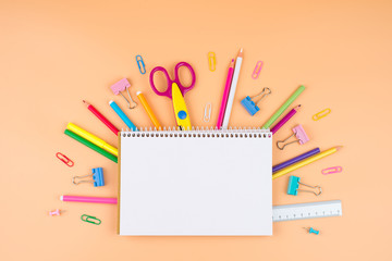 Colorful school supplies over a paper on orange background with place for your text