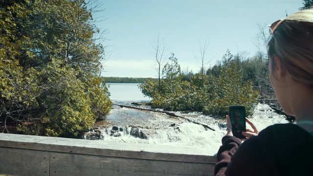 Millennial hiker takes photos of river forest landscape with her phone