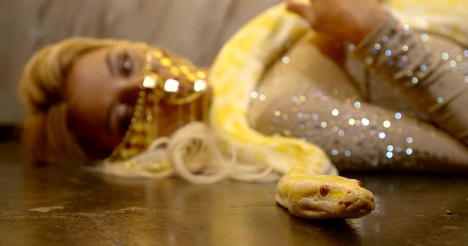 pretty woman and large yellow snake are lying on floor, python is moving to camera