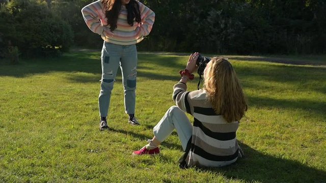 Two young girls taking picture together with camera in grass field