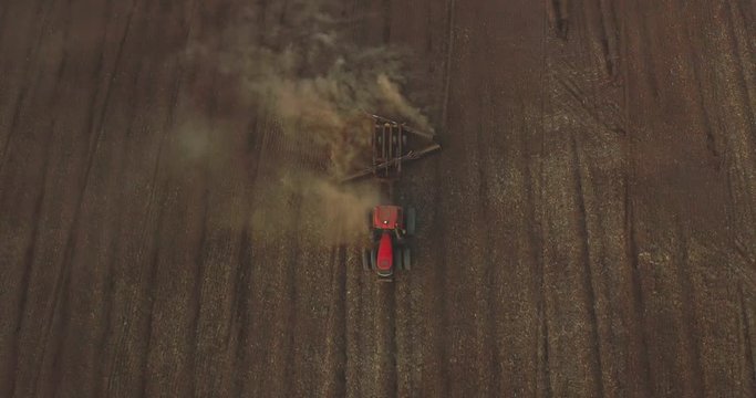 Aerial view of a red tractor tilling soil in a barren landscape at sunset, tractor preparing a field for planting, a new harvest, rural agrarian lifestyle