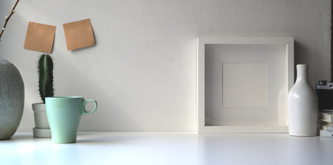 Blank white frame and ceramics jar on a white table against the white wall