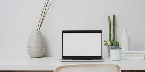 Minimal workspace with open laptop computer and decorations on white table and white wall