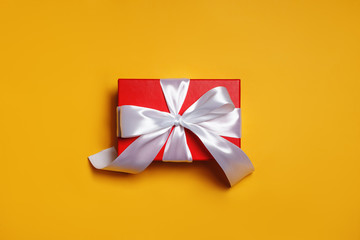 Red box with a gift and a white ribbon on a yellow background