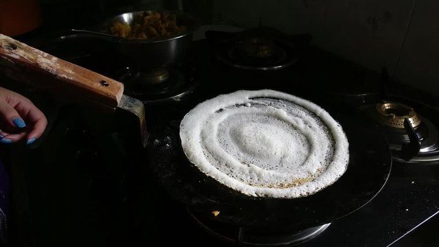 Home made dosa being made by a woman on a old tawa and gas stove with oil and butter, a staple south indian dish this is a popular street food