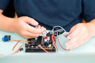 Closeup of a child's hands working with circuits, wires, computer chip, and testing OLED on his robotics project. Science, Technology, Engineering and Mathematics (STEM) education concept. © myboys.me