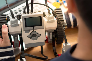 Closeup : hands of preteen / teenage boy codes blocks Mindstorms on his computer laptop, other hand holds robot build for school project. STEM Education, Programming, Robotic Technology, Online Learning