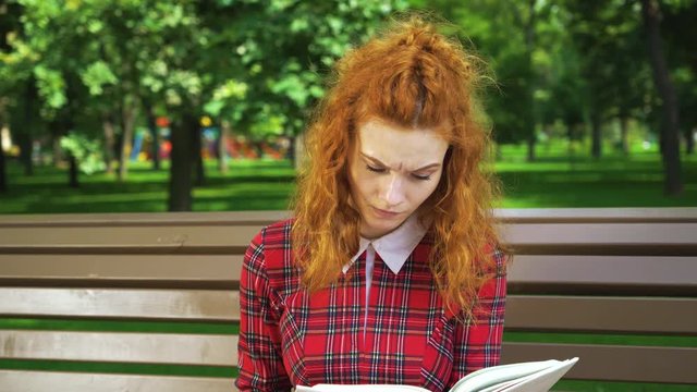 Unhappy Red Haired Girl Reading Thriller In Park