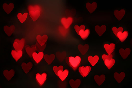 Blurred view of red heart shaped lights on black background