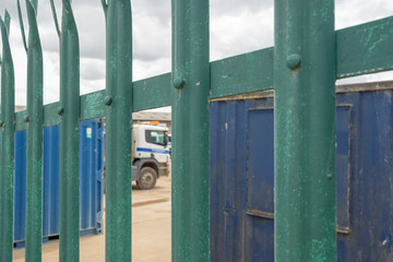 Shallow focus of HGV transport and dumper trucks seen parked in a secure location near a gravel works. The in focus nearby metal fence is spiked for security reasons.