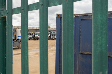 Shallow focus of HGV transport and dumper trucks seen parked in a secure location near a gravel works. The in focus nearby metal fence is spiked for security reasons.