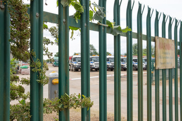 Shallow focus of HGV transport and dumper trucks seen parked in a secure location near a gravel works. The in focus nearby metal fence is spiked for security reasons.