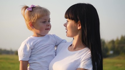 Happy family, mother and child have fun outdoors in the Park. The little lovely blonde girl is having fun and hugs and kisses her mother.