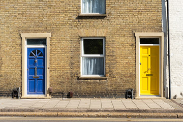 Pair of colourful doors seen on the entrances to old-style terraced houses within a double-yellow road zone. The yellow door has recently been fitted.