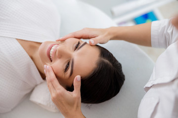 Obraz na płótnie Canvas Cheerful young woman having face massage at beauty salon