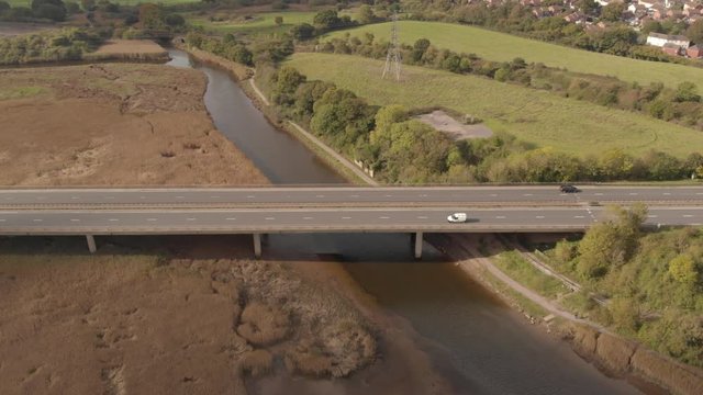Cars driving on long highway over river & marshlands, drone shot