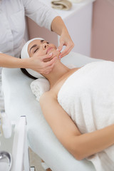 Fototapeta na wymiar Charming young woman enjoying face massage at spa salon