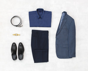 Suit jacket, pants, blue shirt, black shoes, belt, watch on grey background. Overhead view of classic elegant formal men's outfit. Set of stylish men's clothes and accessories. Flat lay, top view.