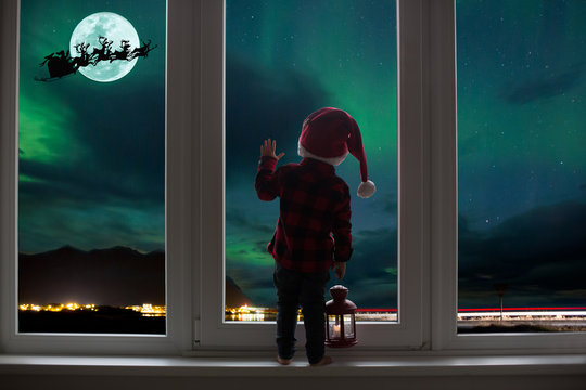 Toddler child standing in front of a big french doors, leaning against it looking out, holding lantern