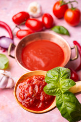 in the foreground, ladle with tomato sauce and fresh basil. Vegetable ingredients in the background.