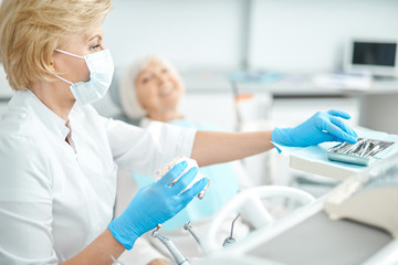 Obraz premium Masked female dentist is taking dental instruments