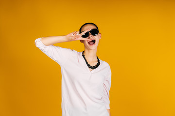 stylish girl makes victory sign with her hands, playfully snapping her tongue. studio yellow