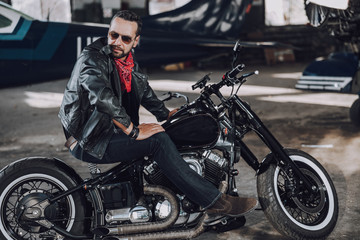 Fototapeta na wymiar Caucasian biker in leather clothes having rest in garage