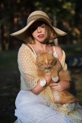 beautiful romantic young woman in a hat is resting in nature with a cat