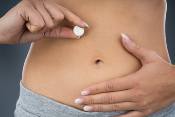 Woman Holding Pill In Front Of Stomach