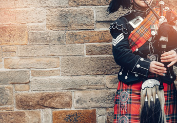 EDINBURGH, SCOTLAND, 24 March 2018 , Scottish bagpiper dressed in traditional red and black tartan dress stand before stone wall. Edinburgh, the most popular tourist city destination in Scotland.. - obrazy, fototapety, plakaty