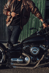 Fototapeta na wymiar Handsome biker with cigar standing near garage outdoors
