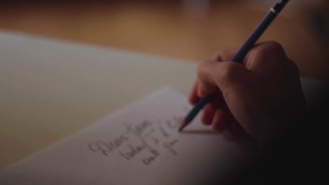 close up su mano che scrive una lettera con una matita su un foglio di carta