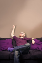 Caucasian Male Sitting on Sofa and Pointing Empty Wall with Copy Space