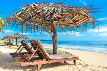 Tropical beautiful beach in Sri Lanka. Ocean and nice sandy shore with beach beds and umbrellas. Sunny view of idyllic and romantic sea beach. Concept of travel, vacation and relax in paradise.