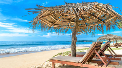 Tropical beach on blue sky background, Sri Lanka. Ocean and nice sandy shore with beach beds and umbrellas. Sunny panorama of idyllic and romantic sea beach. Concept of travel and relax in paradise.