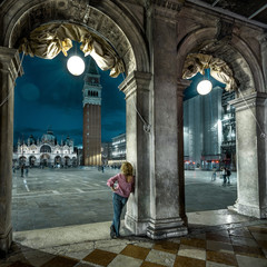 Venice at night, Italy. Young woman is on San Marco square in twilight. Adult girl tourist looks at evening Venice. Vintage architecture of Venice at dusk. Concept of travel and vacation in Venice.