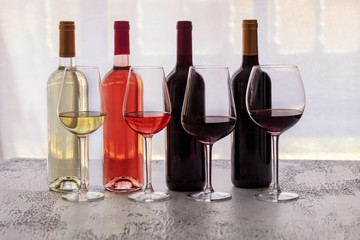 Different wines  bottles red, white, rose and bordeaux with wi9ne glasses on concrete light background. Wine degustation concept. Copy space